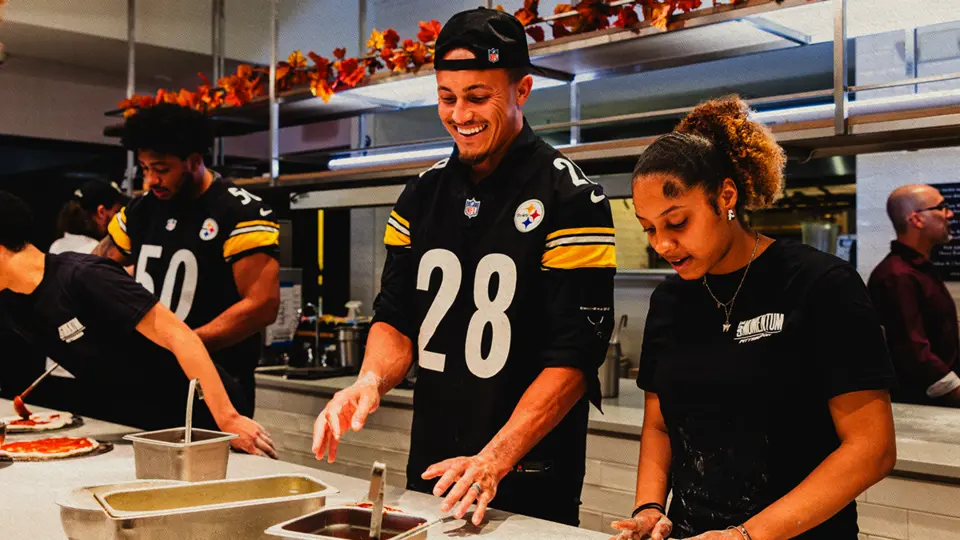 Pittsburgh Steelers players prepare food alongside Café Momentum staff in a kitchen